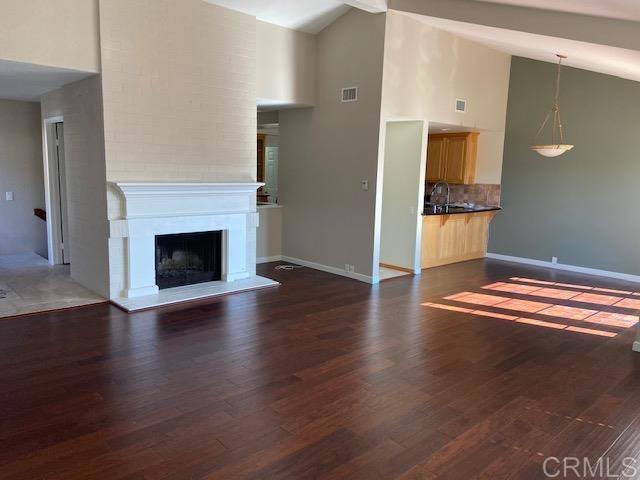 5983 Gaines St, San Diego, CA 92110 - unfurnished living room featuring high vaulted ceiling, dark wood finished floors, and a fireplace with raised hearth