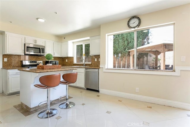 15521 Sandra Ln, Sylmar, CA 91342 - kitchen with stainless steel appliances, white cabinets, tasteful backsplash, a kitchen island, and a breakfast bar