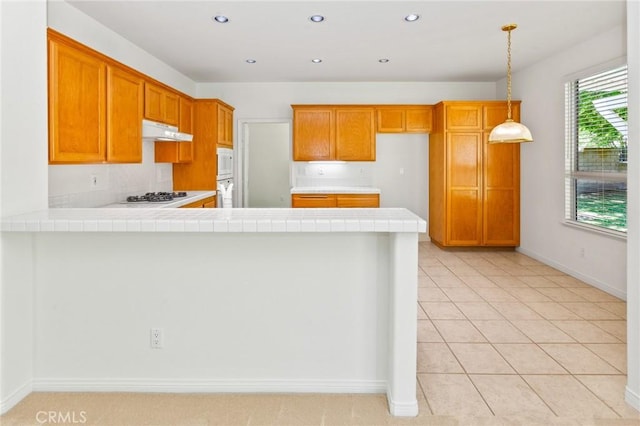 2311 Gillingham Cir, Thousand Oaks, CA 91362 - kitchen featuring tile counters, under cabinet range hood, brown cabinetry, a peninsula, and gas cooktop