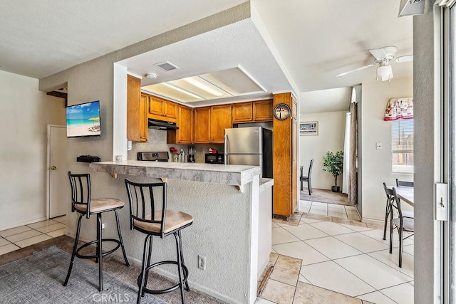 2134 Moonlight Ct, Palmdale, CA 93550 - kitchen featuring freestanding refrigerator, under cabinet range hood, light tile patterned flooring, brown cabinets, and a peninsula