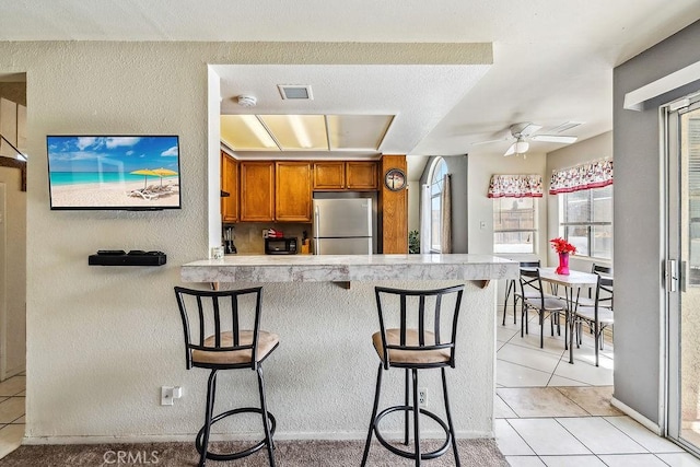 2134 Moonlight Ct, Palmdale, CA 93550 - kitchen with freestanding refrigerator, brown cabinets, light tile patterned floors, light countertops, and a textured wall