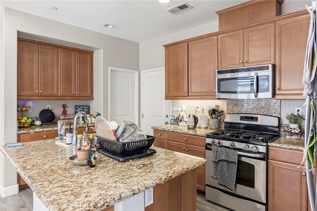 15530 Bonsai Way, Tustin, CA 92782 - kitchen with appliances with stainless steel finishes, light wood-type flooring, light stone counters, and an island with sink