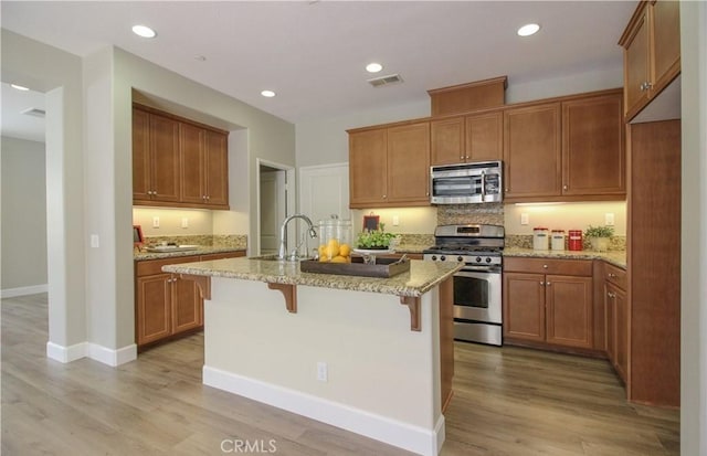 15530 Bonsai Way, Tustin, CA 92782 - kitchen featuring stainless steel appliances, light stone counters, a kitchen breakfast bar, an island with sink, and light wood-style floors