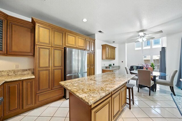 18103 Smokesignal Dr, San Diego, CA 92127 - kitchen featuring freestanding refrigerator, brown cabinetry, a ceiling fan, a center island, and light stone countertops