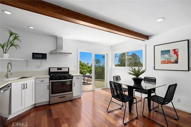 10255 Overhill Dr, Santa Ana, CA 92705 - kitchen featuring appliances with stainless steel finishes, wall chimney range hood, light countertops, beamed ceiling, and wood finished floors