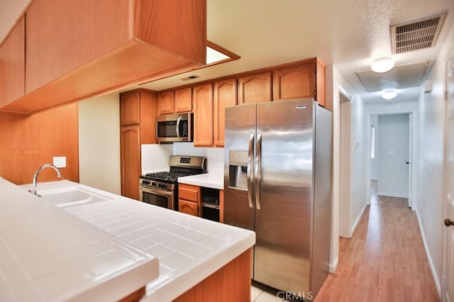 11600 Warner Ave Unit 428, Fountain Valley, CA 92708 - kitchen featuring stainless steel appliances, tile counters, brown cabinetry, and tasteful backsplash