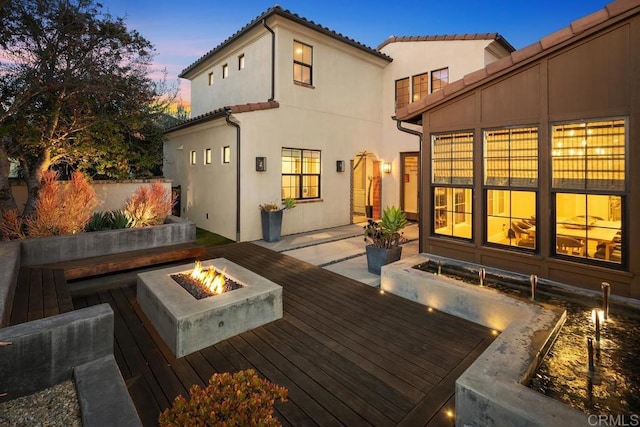 15614 S Chevy Chase, San Diego, CA 92127 - back of property at dusk featuring an outdoor fire pit, a wooden deck, stucco siding, and a tile roof