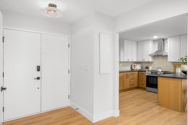 10437 Hermanos Rd, San Diego, CA 92124 - kitchen with stainless steel electric range, wall chimney exhaust hood, dark countertops, light wood-type flooring, and backsplash