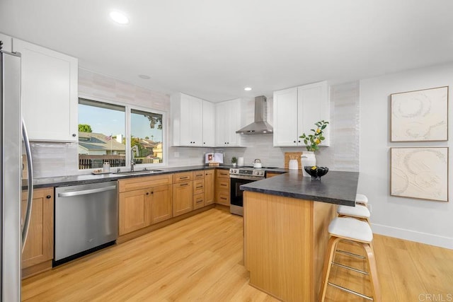 10437 Hermanos Rd, San Diego, CA 92124 - kitchen featuring stainless steel appliances, wall chimney range hood, a kitchen breakfast bar, decorative backsplash, and light wood finished floors