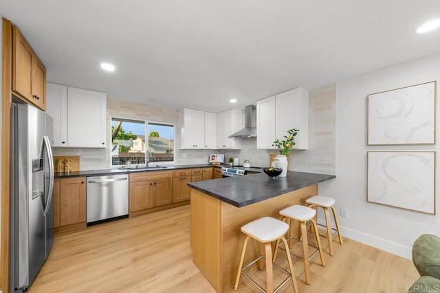 10437 Hermanos Rd, San Diego, CA 92124 - kitchen with stainless steel appliances, wall chimney range hood, a peninsula, light wood finished floors, and backsplash