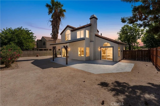 37921 Tackstem St, Palmdale, CA 93552 - back of property at dusk with a patio area, stucco siding, a chimney, a fenced backyard, and a tiled roof