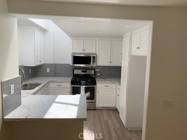 363 Cleo St, Laguna Beach, CA 92651 - kitchen featuring stainless steel appliances, light wood-type flooring, white cabinetry, backsplash, and light stone counters