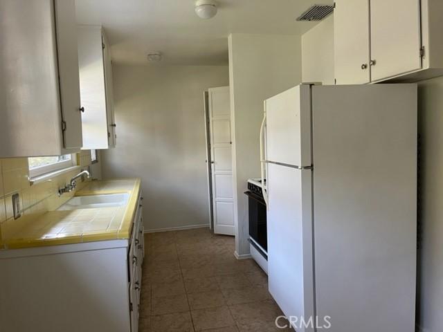 10856 Camarillo St, Toluca Lake, CA 91602 - kitchen with freestanding refrigerator, tile countertops, white cabinets, range, and backsplash
