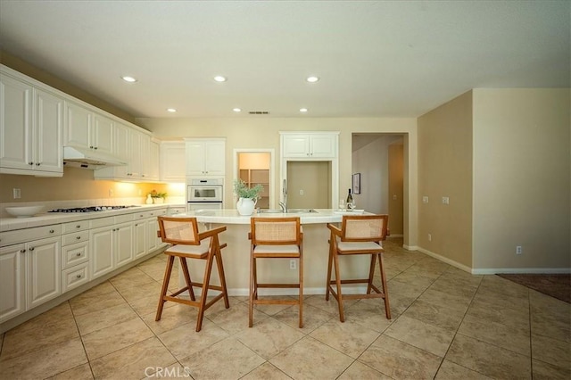 25217 Pacific Crest St, Corona, CA 92883 - kitchen with under cabinet range hood, gas stovetop, a center island with sink, light tile patterned floors, and white cabinetry