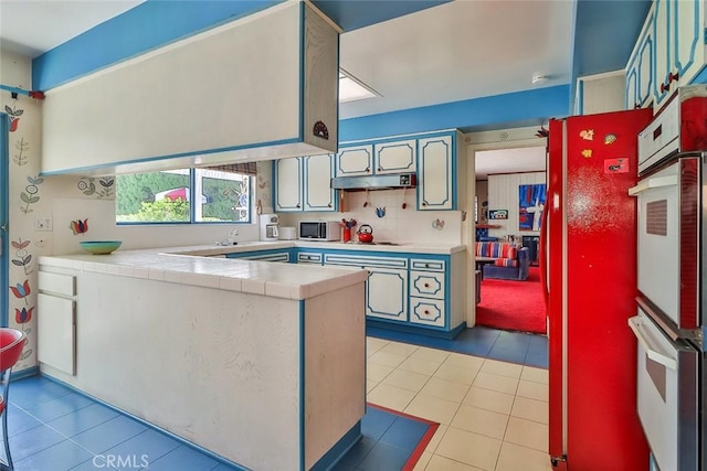 17313 Citronia St, Northridge, CA 91325 - kitchen with tile countertops, a peninsula, light tile patterned flooring, and under cabinet range hood