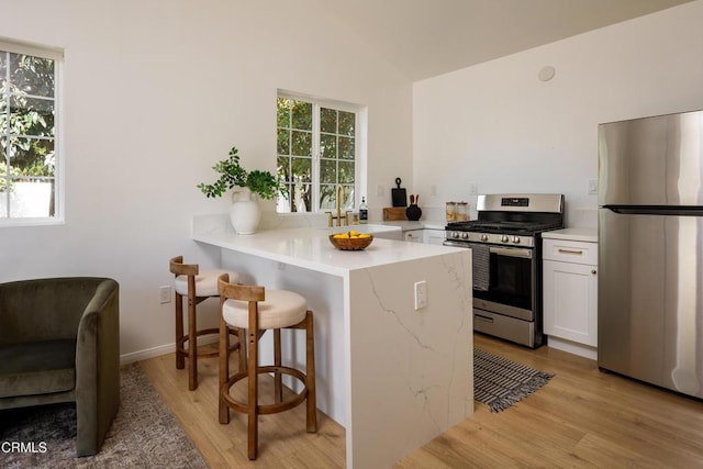221 N 7th St, Santa Paula, CA 93060 - kitchen featuring stainless steel appliances, a kitchen bar, light wood-type flooring, white cabinets, and a peninsula