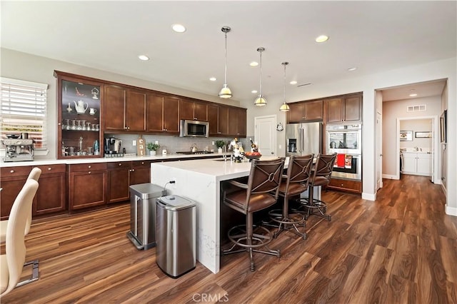 27843 Huron Ct, Menifee, CA 92585 - kitchen featuring appliances with stainless steel finishes, dark wood-style floors, light countertops, a kitchen breakfast bar, and a kitchen island with sink