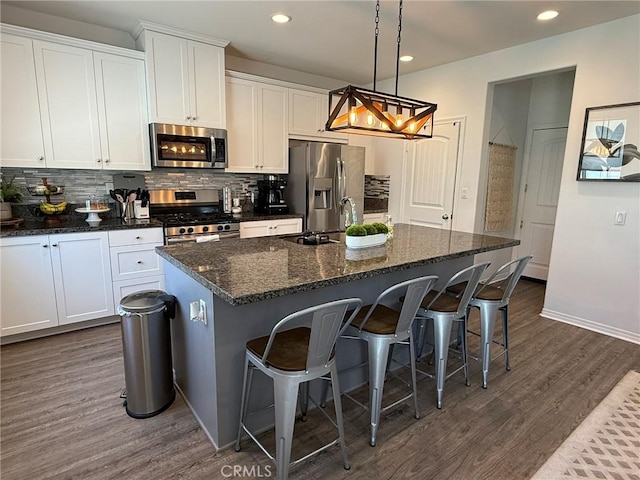 27265 Graphite Dr, Menifee, CA 92584 - kitchen featuring appliances with stainless steel finishes, dark wood finished floors, a kitchen island with sink, decorative backsplash, and recessed lighting