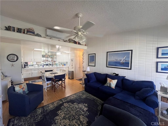 1271 Kenwood Rd Unit M7-J, Seal Beach, CA 90740 - living room with a ceiling fan, a wall mounted AC, light wood-type flooring, and a textured ceiling
