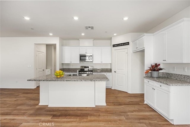7305 Scrivia Ct, Bakersfield, CA 93311 - kitchen with stainless steel microwave, white cabinetry, an island with sink, light wood-style flooring, and recessed lighting
