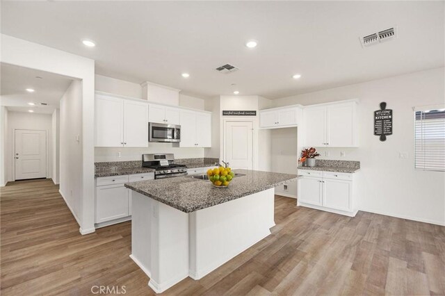 7305 Scrivia Ct, Bakersfield, CA 93311 - kitchen with stainless steel appliances, white cabinetry, light wood-style floors, a center island with sink, and recessed lighting