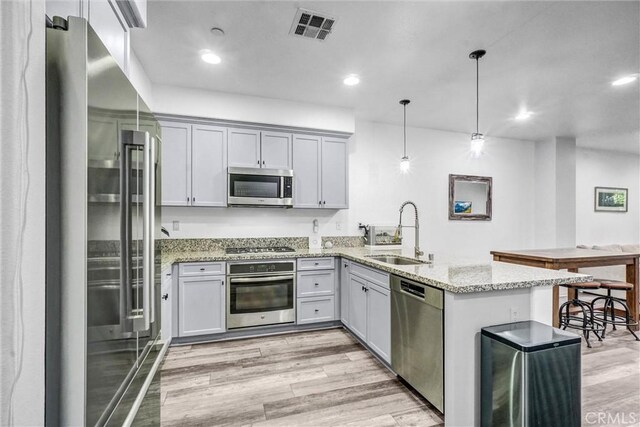 17035 Independence Way, Yorba Linda, CA 92886 - kitchen featuring appliances with stainless steel finishes, a peninsula, light wood-style floors, light stone counters, and decorative light fixtures