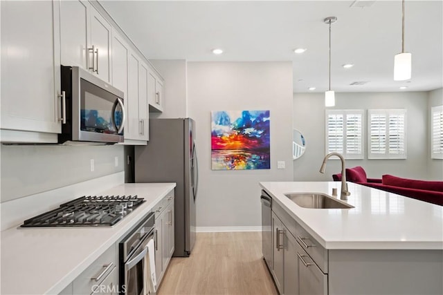 27753 Dyer Way, Canyon Country, CA 91387 - kitchen with appliances with stainless steel finishes, light countertops, light wood-type flooring, an island with sink, and hanging light fixtures