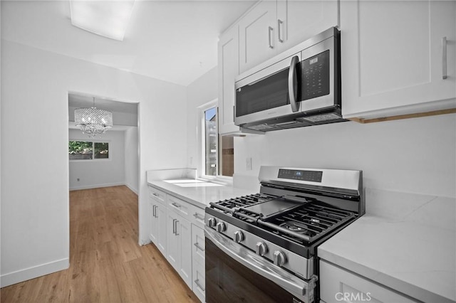 7848 Chastain Ave, Reseda, CA 91335 - kitchen with appliances with stainless steel finishes, white cabinets, light countertops, light wood-style floors, and a chandelier