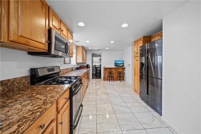 42903 Normandy Ln, Lancaster, CA 93536 - kitchen featuring stainless steel appliances, light marble finish flooring, dark stone countertops, brown cabinetry, and recessed lighting