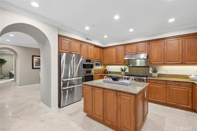 2 Tarascon, Newport Coast, CA 92657 - kitchen with appliances with stainless steel finishes, under cabinet range hood, light stone counters, arched walkways, and brown cabinets