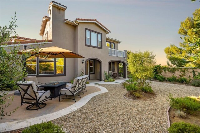 2 Tarascon, Newport Coast, CA 92657 - back of house at dusk with a balcony, an outdoor fire pit, stucco siding, a patio area, and a tile roof