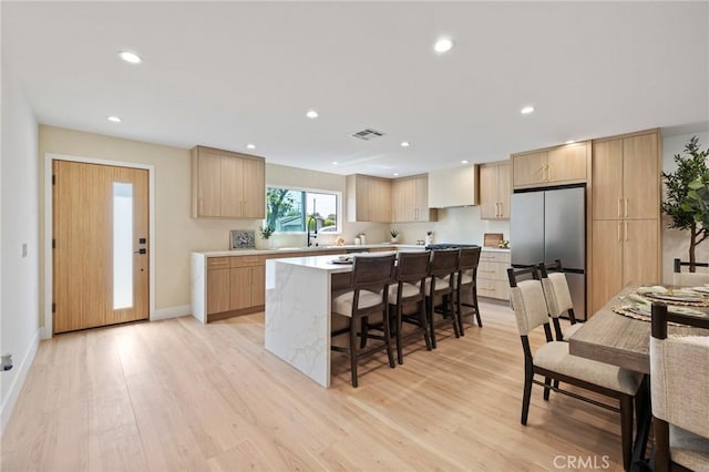 8840 Valjean Ave, North Hills, CA 91343 - kitchen with freestanding refrigerator, a center island, a breakfast bar, light wood-style floors, and light brown cabinetry