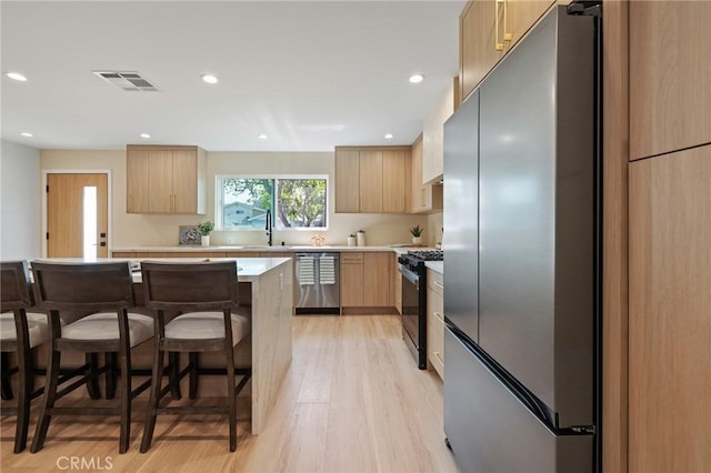 8840 Valjean Ave, North Hills, CA 91343 - kitchen featuring appliances with stainless steel finishes, light brown cabinetry, a kitchen breakfast bar, light countertops, and light wood-type flooring