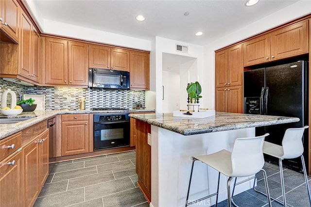 5410 W 149th Pl Unit 12, Hawthorne, CA 90250 - kitchen with black appliances, a breakfast bar, light stone counters, a center island, and tasteful backsplash