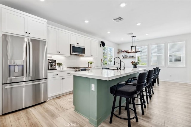 10 Wisteria St, Rancho Mission Viejo, CA 92694 - kitchen with appliances with stainless steel finishes, light wood finished floors, light countertops, white cabinetry, and an island with sink