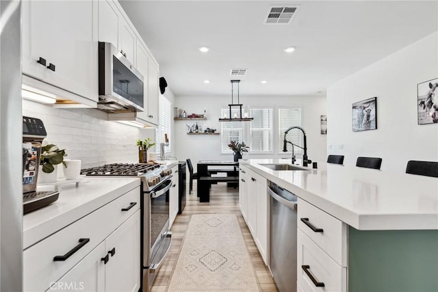 10 Wisteria St, Rancho Mission Viejo, CA 92694 - kitchen featuring appliances with stainless steel finishes, light countertops, white cabinets, light wood-type flooring, and an island with sink