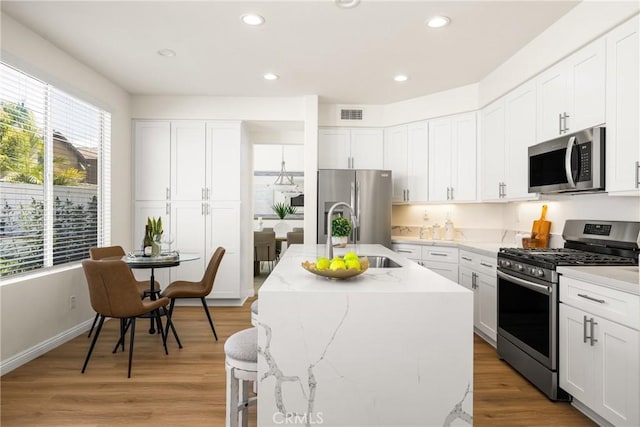 17 Marseille Way, Lake Forest, CA 92610 - kitchen with stainless steel appliances, light stone counters, a kitchen island with sink, light wood finished floors, and white cabinetry
