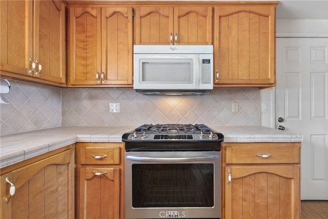 35632 Avocado St, Yucaipa, CA 92399 - kitchen featuring stainless steel range with gas stovetop, white microwave, tile counters, decorative backsplash, and brown cabinets