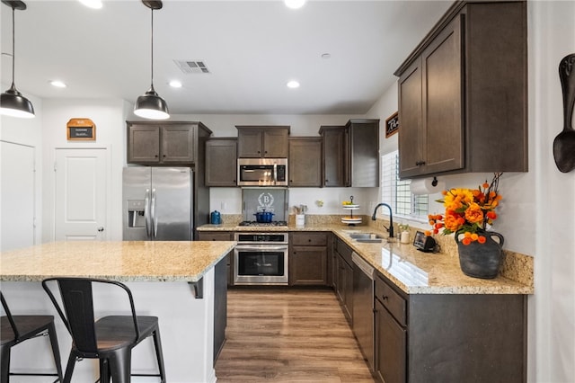 24212 Bay Laurel Ave, Murrieta, CA 92562 - kitchen with appliances with stainless steel finishes, dark brown cabinets, light wood finished floors, a breakfast bar, and light stone counters