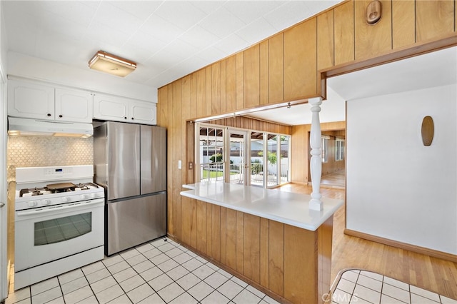 2460 Vuelta Grande Ave, Long Beach, CA 90815 - kitchen with freestanding refrigerator, white range with gas stovetop, under cabinet range hood, white cabinetry, and wooden walls
