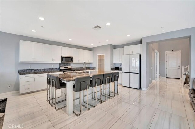 18348 Cachet Way, Canyon Country, CA 91350 - kitchen featuring stainless steel appliances, a kitchen breakfast bar, an island with sink, white cabinetry, and dark stone countertops