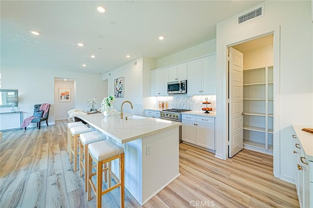 27505 Illumination Ct, Valencia, CA 91381 - kitchen with appliances with stainless steel finishes, light wood-style floors, white cabinets, a kitchen breakfast bar, and recessed lighting