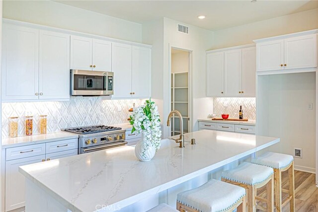 27505 Illumination Ct, Valencia, CA 91381 - kitchen featuring appliances with stainless steel finishes, white cabinets, an island with sink, light wood-style flooring, and recessed lighting