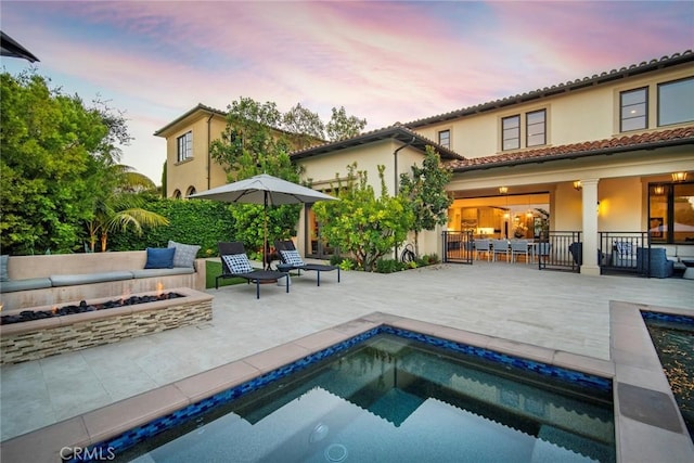16 Seawatch, Newport Coast, CA 92657 - back of property at dusk with an outdoor fire pit, a patio, stucco siding, and an outdoor pool