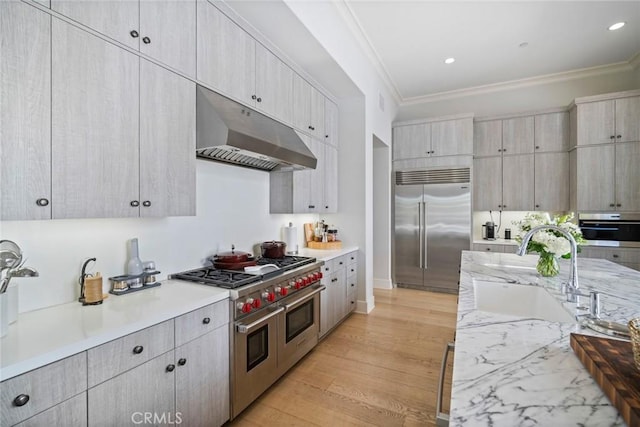 16 Seawatch, Newport Coast, CA 92657 - kitchen featuring high end appliances, under cabinet range hood, ornamental molding, light wood-type flooring, and light stone countertops