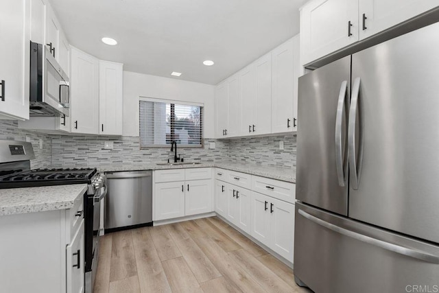 7528 Jerez Ct Unit 6, Carlsbad, CA 92009 - kitchen featuring appliances with stainless steel finishes, light wood-type flooring, backsplash, white cabinetry, and light stone countertops