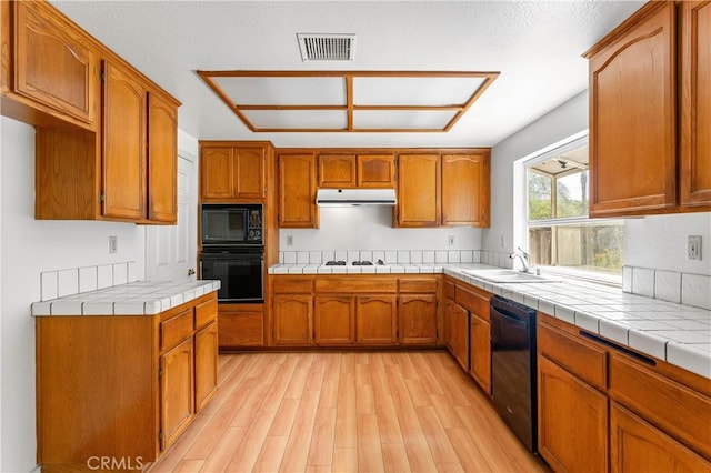44051 Sheldon Ct, Temecula, CA 92592 - kitchen featuring black appliances, light wood-style floors, under cabinet range hood, brown cabinets, and tile countertops