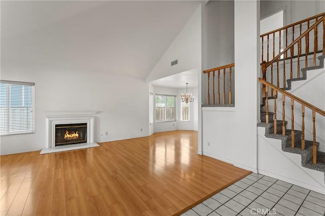 44051 Sheldon Ct, Temecula, CA 92592 - unfurnished living room with a chandelier, a glass covered fireplace, wood finished floors, stairway, and high vaulted ceiling