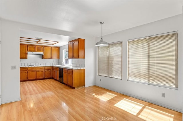 44051 Sheldon Ct, Temecula, CA 92592 - kitchen featuring under cabinet range hood, dishwasher, brown cabinets, gas stovetop, and pendant lighting
