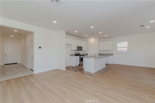 24679 Acadia Dr, Corona, CA 92883 - kitchen with appliances with stainless steel finishes, white cabinets, light wood-type flooring, open floor plan, and a kitchen island with sink